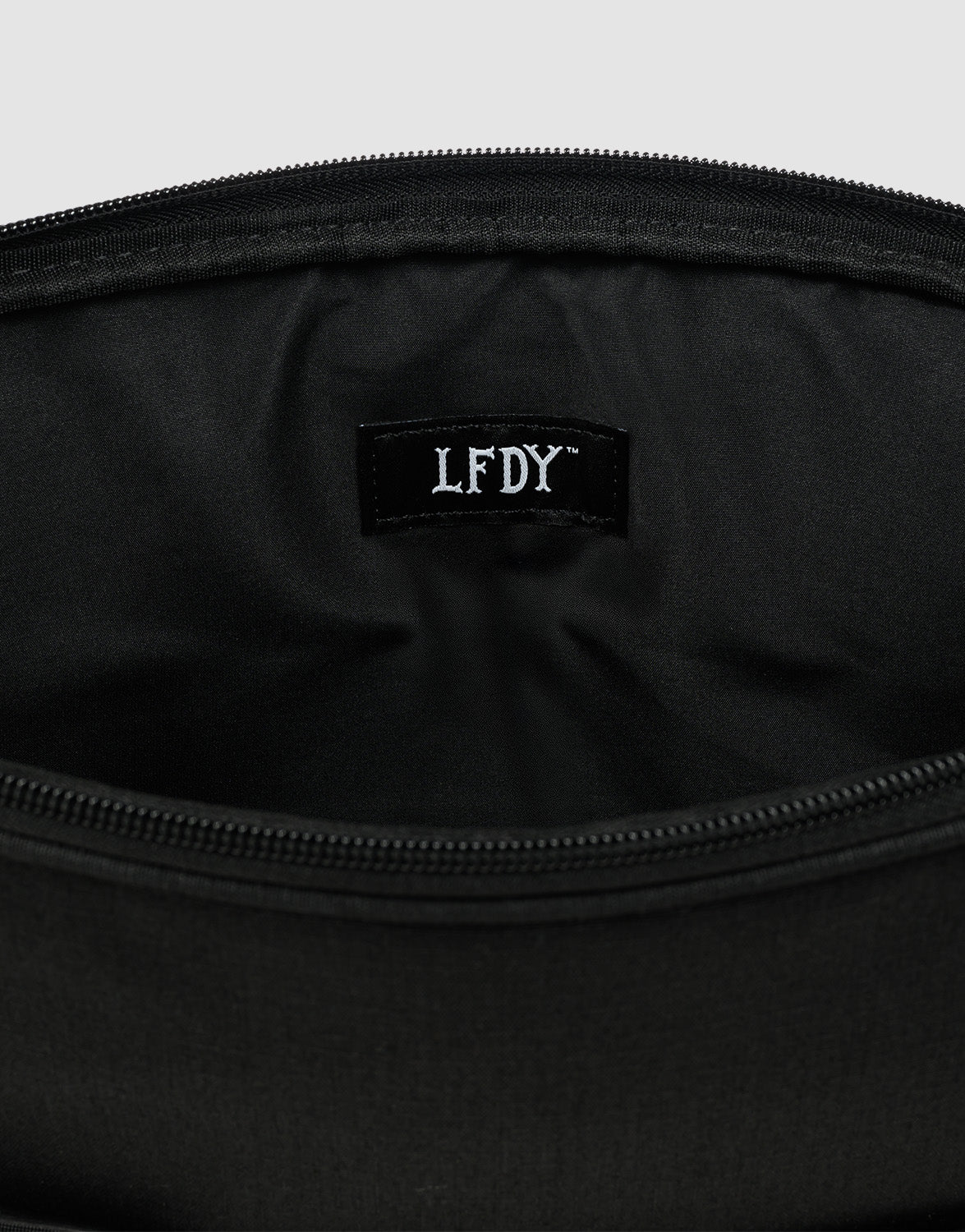 A close-up of the LFDY Laptop Case by LIVE FAST DIE YOUNG reveals its black polyester exterior, a black fabric label with white "LFDY" text, and a practical Laptopfach for enhanced functionality.