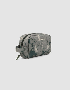 The LFDY Amenity Kit by LIVE FAST DIE YOUNG is a small rectangular toiletry bag with a camouflage pattern, 100% polyester, large zipper compartment, side handle, and “LIVE FAST” printed on the front. Plain light gray background.