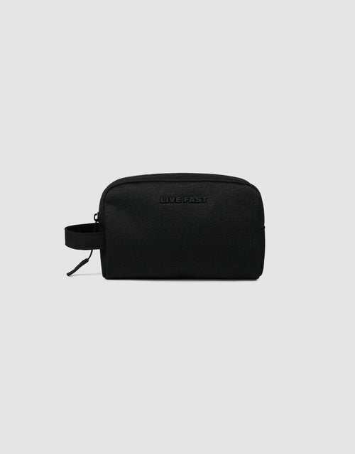 The LFDY Amenity Kit by LIVE FAST DIE YOUNG is a black polyester zip pouch with a side handle, "LIVE FAST" embossed on the front, a large zip compartment, and inner pockets, shown on a plain light gray background.