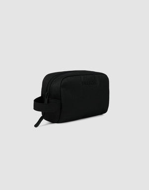 The LFDY Amenity Kit by LIVE FAST DIE YOUNG is a black rectangular toiletry bag made from durable polyester with a zipper closure, side handle, and large zip pocket, shown against a light gray background.