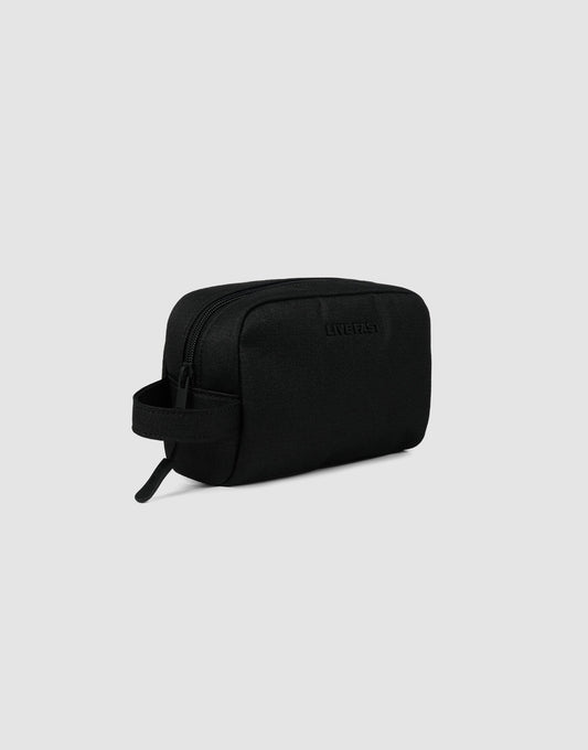 The LFDY Amenity Kit by LIVE FAST DIE YOUNG is a black rectangular toiletry bag made from durable polyester with a zipper closure, side handle, and large zip pocket, shown against a light gray background.
