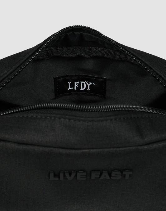 A close-up of the LFDY Amenity Kit by LIVE FAST DIE YOUNG—a black polyester zippered bag with "LIVE FAST" embossed outside and an LFDY label inside, partially open to show its inner pockets and large zip compartment.