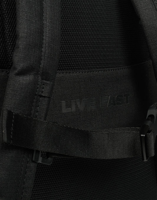 Close-up of the black LFDY Backpack (19L) by LIVE FAST DIE YOUNG, with "LIVE FAST" subtly printed on the fabric, partially covered by a strap and plastic buckle, and featuring adjustable shoulder straps for comfort.