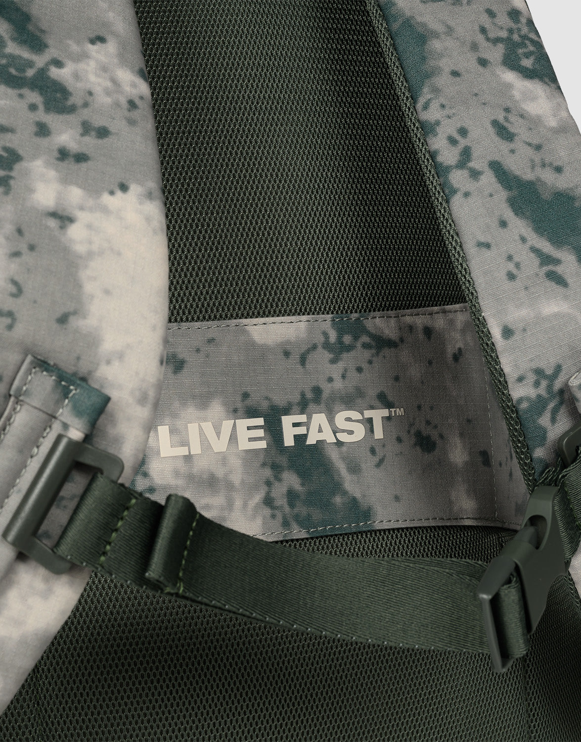 Close-up of the LFDY Travel Backpack by LIVE FAST DIE YOUNG, a green and gray camo 25L rucksack featuring a mesh panel, adjustable shoulder straps, and an inner label reading "LIVE FAST" in bold white letters.