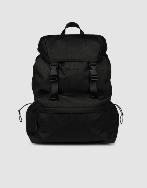 The LFDY Travel Backpack by LIVE FAST DIE YOUNG is a black 25L rucksack featuring adjustable shoulder straps, a top flap, two front buckles, side drawstring pockets, and a top handle, shown against a plain light gray background.