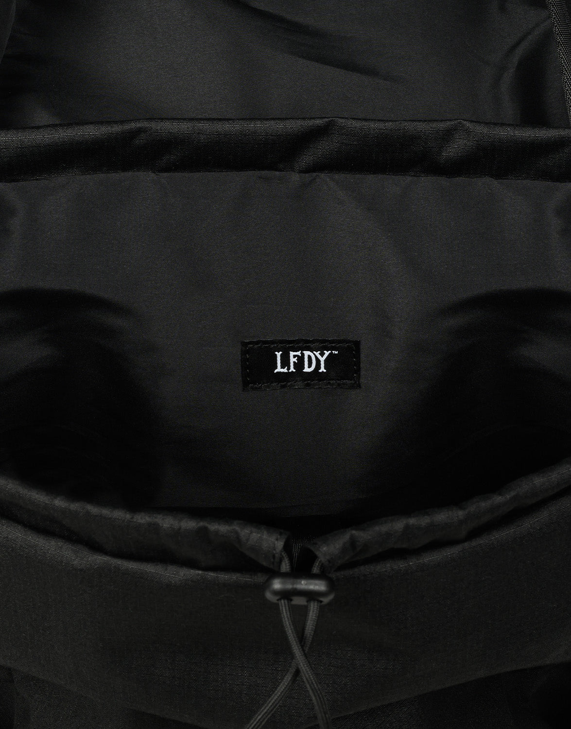 Close-up of the LFDY Travel Backpack by LIVE FAST DIE YOUNG, showing its black interior with a stitched white LFDY label in gothic font. Features a 25-liter capacity and adjustable shoulder straps for comfort.