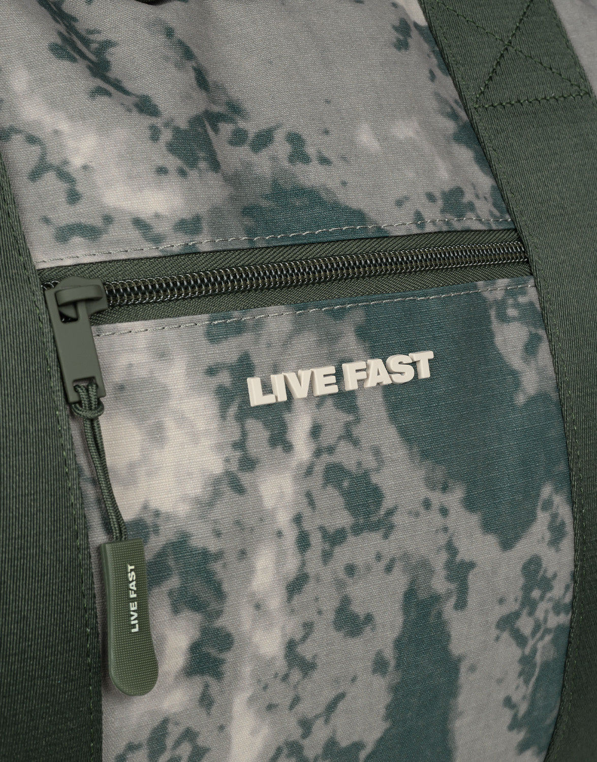 Close-up of the LFDY Weekender 60 by LIVE FAST DIE YOUNG, showing a zippered pocket with green and gray camo fabric and "LIVE FAST" in white above the zipper. The padded Schultergurt ensures comfort, ideal for use as a compact Sporttasche.