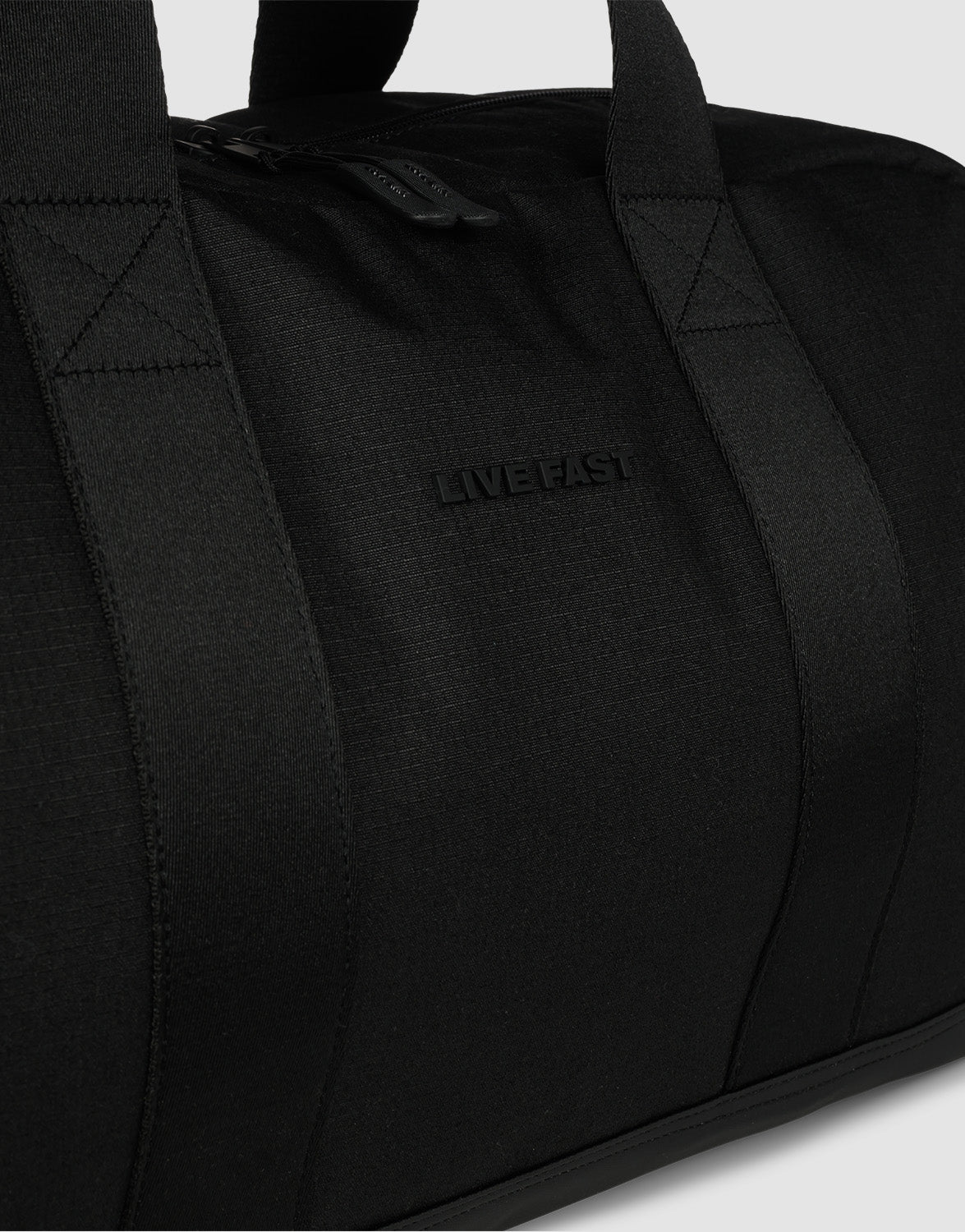 A close-up of a black 50L LFDY Weekender duffel by LIVE FAST DIE YOUNG, featuring sturdy handles, "LIVEFAST" embossed on the front, textured polyester material, top zipper closure, and a detachable shoulder strap for easy carrying.