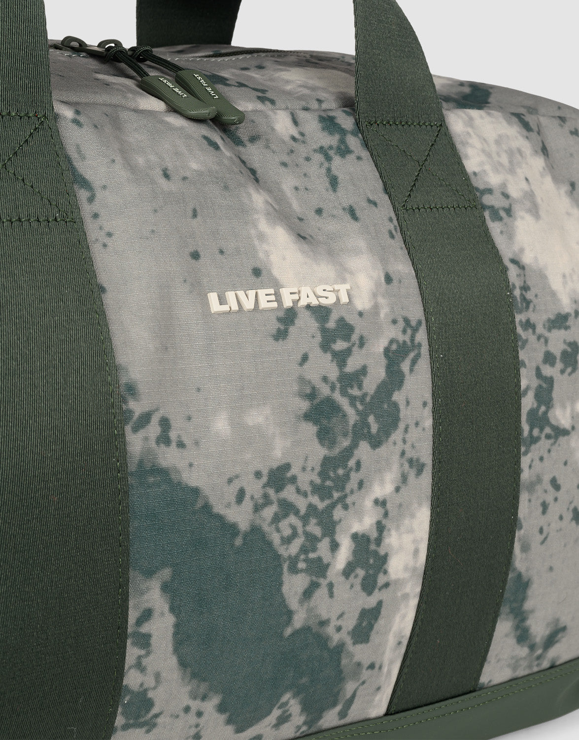Close-up of the LFDY Weekender 50 by LIVE FAST DIE YOUNG, a 50L duffel bag with dark green straps and gray-green marbled design. "LIVE FAST" is printed in white near the top. Includes an abnehmbarer Schultergurt for easy carrying.
