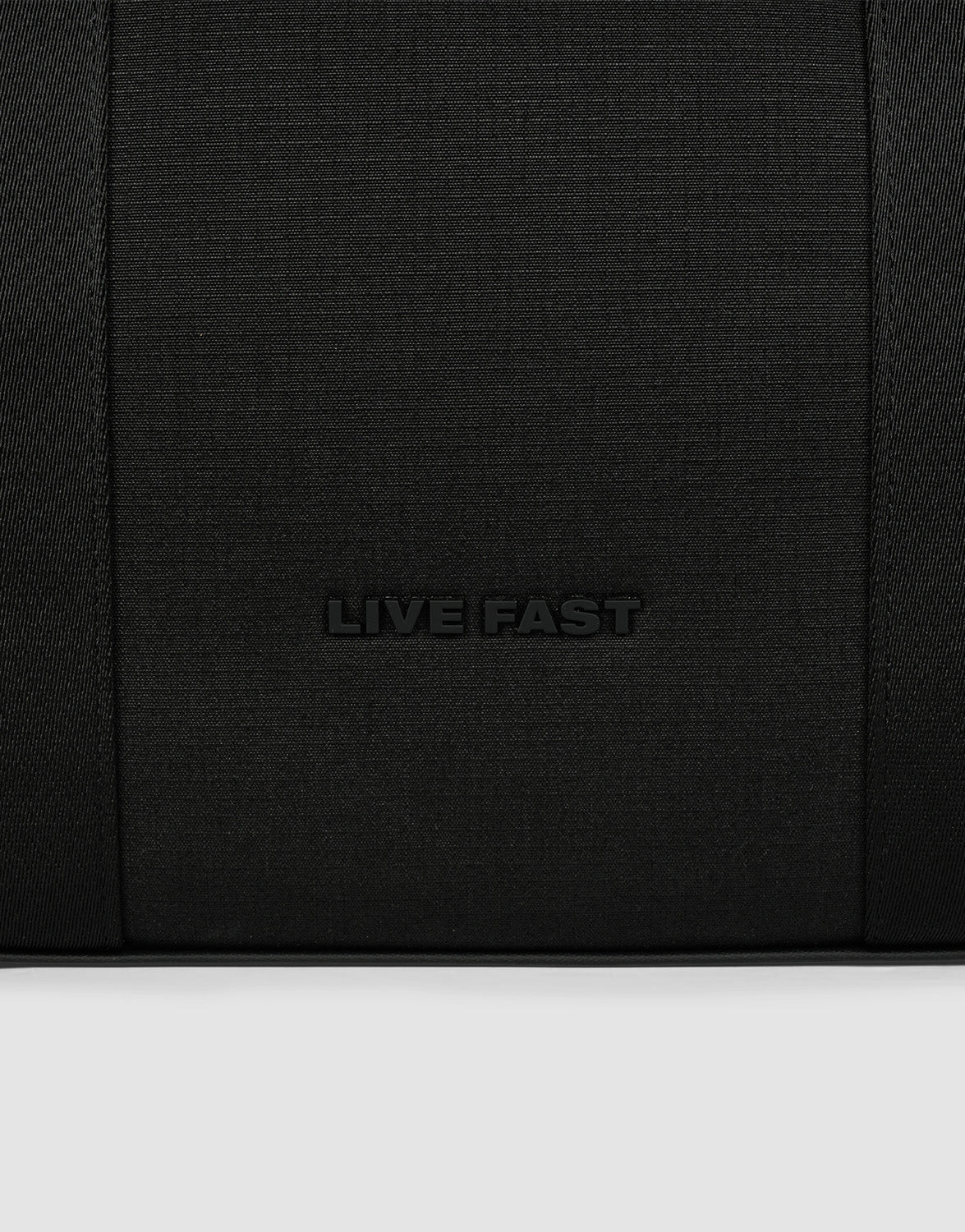 A close-up of black textured polyester from the LFDY Utility Bag by LIVE FAST DIE YOUNG, featuring "LIVE FAST" embossed in the center and hinting at its großes Fach for practical use.