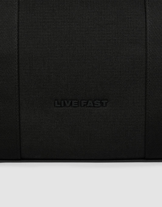 A close-up of black textured polyester from the LFDY Utility Bag by LIVE FAST DIE YOUNG, featuring "LIVE FAST" embossed in the center and hinting at its großes Fach for practical use.