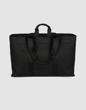 The LFDY Utility Bag by LIVE FAST DIE YOUNG is a large black tote with two short handles, two long shoulder straps, a spacious main compartment, and durable polyester construction, shown against a plain light gray background.