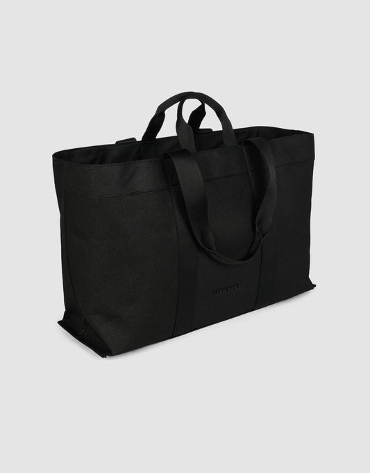 The LFDY Utility Bag by LIVE FAST DIE YOUNG is a large black canvas tote with two short handles, two long shoulder straps, and a spacious main compartment, shown against a plain light gray background.