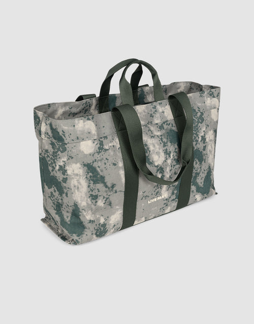 The LFDY Utility Bag by LIVE FAST DIE YOUNG is a spacious tote with sturdy dark green handles and an abstract gray, white, and green pattern. Pictured on a plain light background, it’s angled to show its front and side.