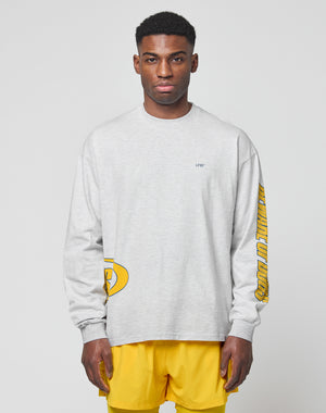 A man faces forward in a LIVE FAST DIE YOUNG LFDY Split Sphere Longsleeve—a light gray, oversized shirt with yellow designs and LIVIN text on the chest—paired with bright yellow shorts against a plain light background.