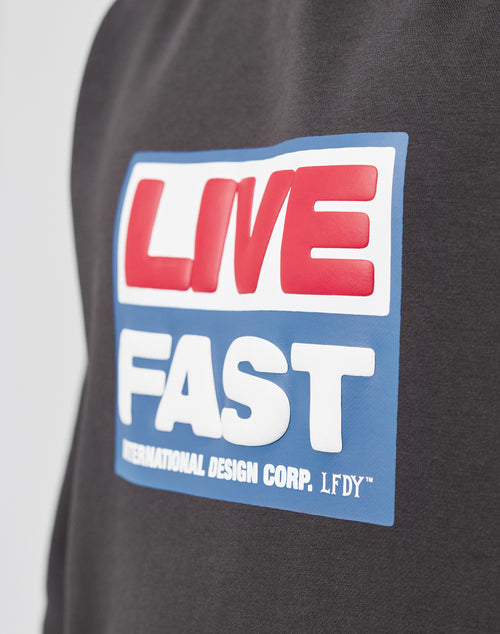 Close-up of the LIVE FAST DIE YOUNG Live Fast Box Hooded sweatshirt, oversized fit, featuring a puffer print reading LIVE in red on white and FAST in white on blue, with INTERNATIONAL DESIGN CORP. LFDY™ below.