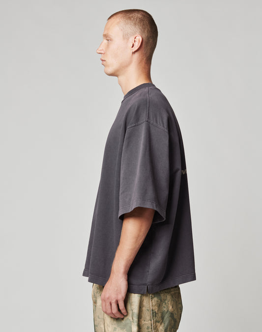 A man with short hair stands in profile against a plain background, wearing the LIVE FAST DIE YOUNG Live Fast Cropped Oversized Tee and light camouflage-patterned pants.