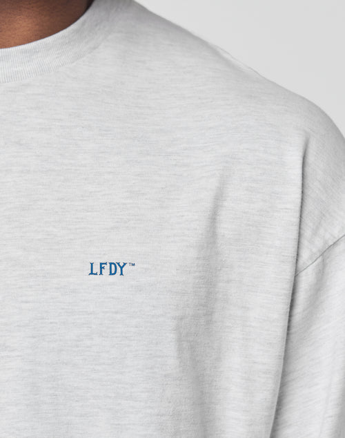 Close-up of a person wearing the LFDY Split Sphere Longsleeve by LIVE FAST DIE YOUNG in light grey, featuring blue LFDY™ embroidery on the left chest. Only part of the neck, shoulder, and upper chest are visible.
