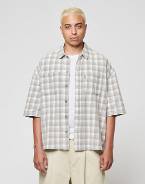 A person with short bleached blonde hair wears the LFDY Light Flannel by LIVE FAST DIE YOUNG in grey and white vintage wash over a white T-shirt and beige pants, standing against a plain light background.