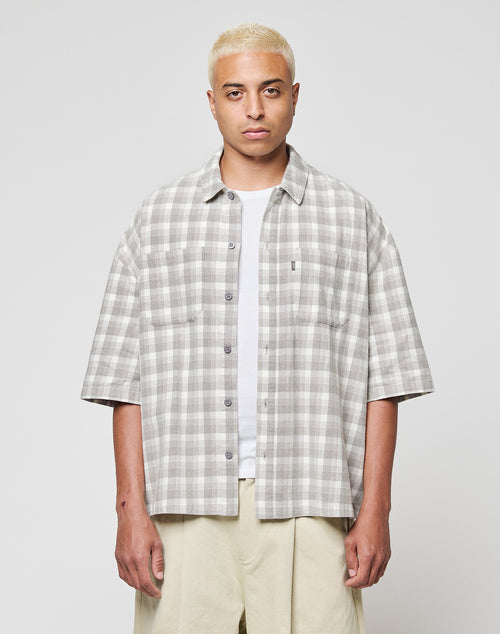 A person with short bleached blonde hair wears the LFDY Light Flannel by LIVE FAST DIE YOUNG in grey and white vintage wash over a white T-shirt and beige pants, standing against a plain light background.