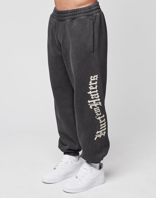 A person wears wide fit black LFDY Haters Jogger sweatpants by LIVE FAST DIE YOUNG, featuring Warren Lotas in bold white gothic letters on one leg, eingrifftaschen, elastikbund, and paired with white sneakers against a light background.