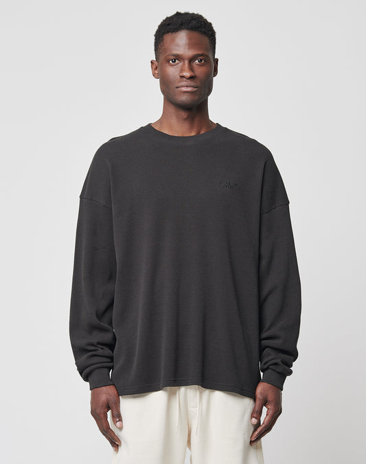 A man stands facing forward, wearing the LIVE FAST DIE YOUNG Basic Waffle Longsleeve in black with logo embroidery and light pants against a plain, light gray background.