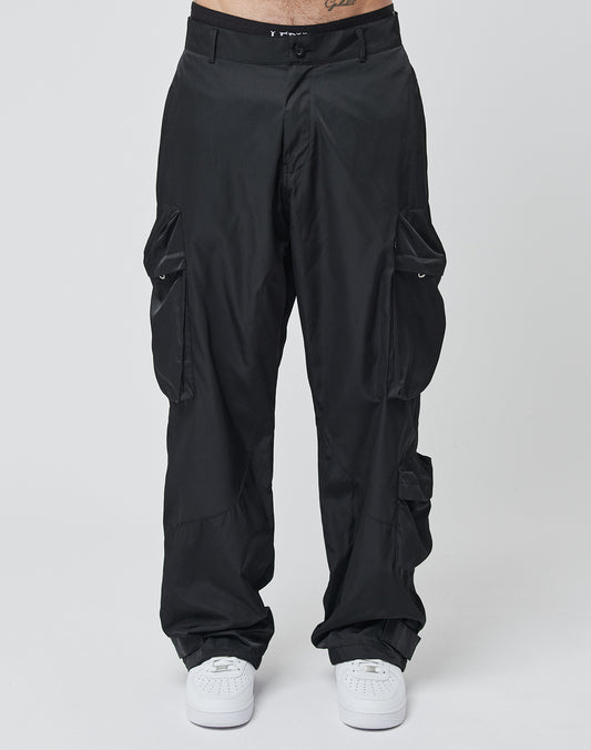 Someone in LIVE FAST DIE YOUNG’s Nylon Cargo pants—loose-fit black cargos with adjustable features, made from durable polyester—paired with white sneakers, stands against a plain light background.