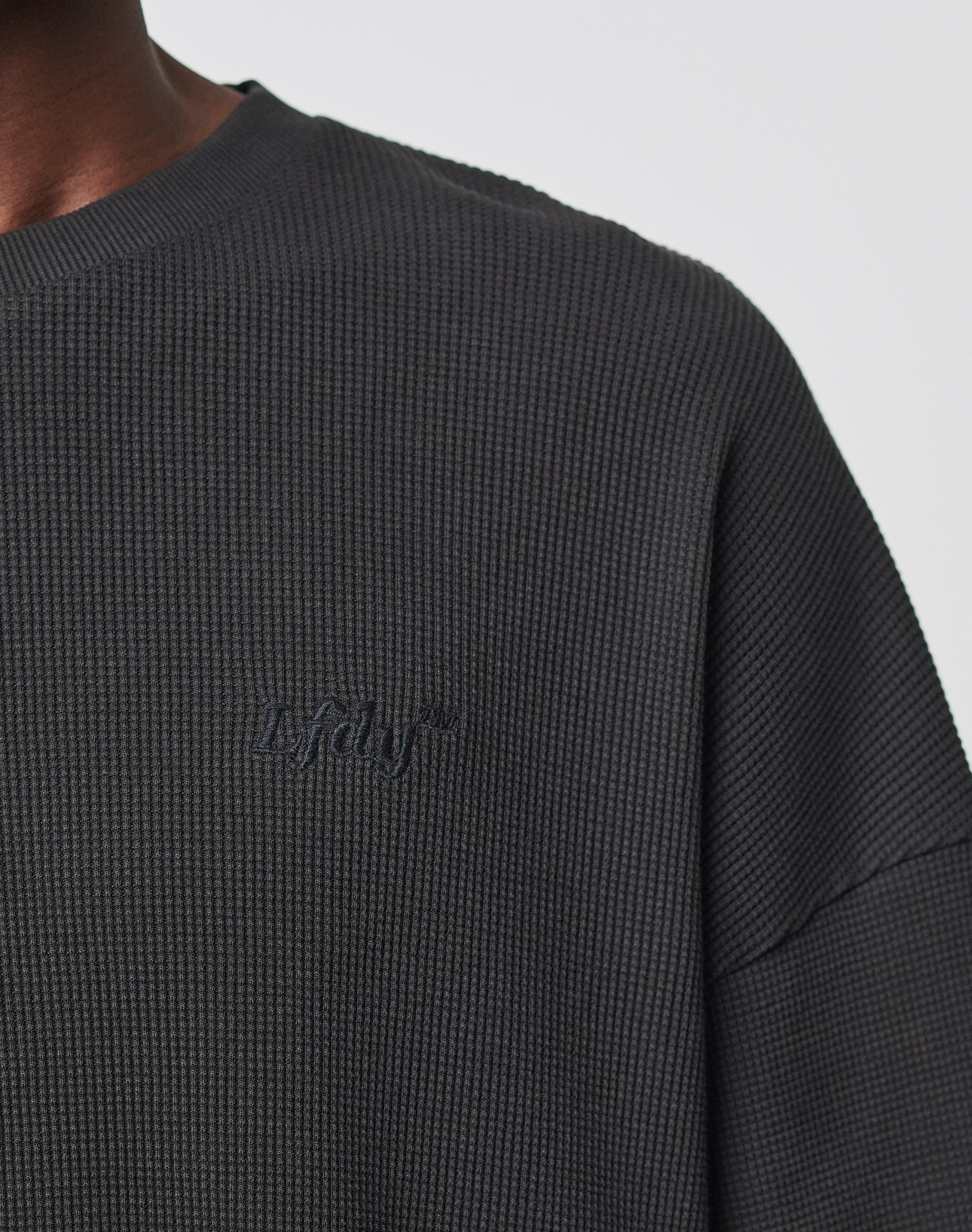 Close-up of the shoulder and neck area of a person wearing the Basic Waffle Longsleeve by LIVE FAST DIE YOUNG, featuring a textured dark gray waffle-knit fabric and subtle lafay Logo-Stick embroidery on the chest.