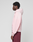 A person stands in profile against a plain light background, wearing the LIVE FAST DIE YOUNG Basic Evidence Hooded Zip in light pink with an oversize fit and maroon pants. Their hands are relaxed at their sides, hood down.