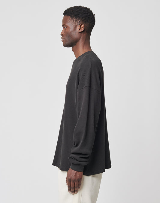 A man in profile against a plain light background wears LIVE FAST DIE YOUNGs Basic Waffle Longsleeve in black with a subtle logo-stitch, made from 100% cotton, paired with light-colored pants.