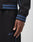 A close-up shows a person in the LIVE FAST DIE YOUNG Live Fast Tracksuit Jacket, black with blue-striped cuffs and waistband, Raglan sleeves, and Live Fast with a subtle blue logo embroidered on the pants. Their hand rests by their side.