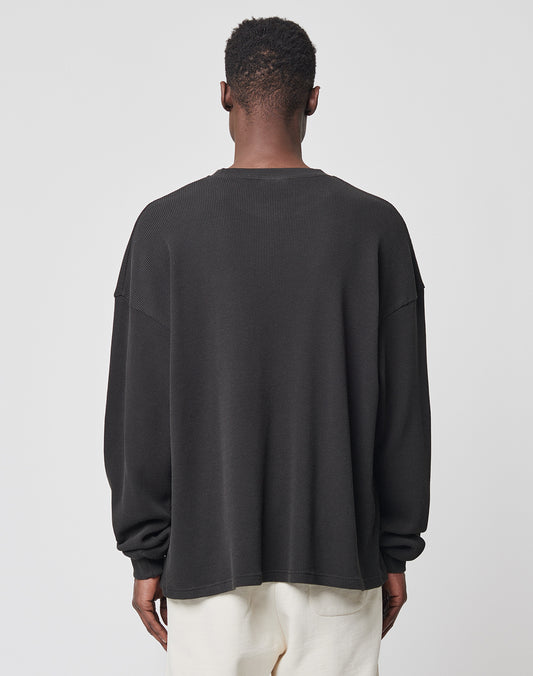 A person with short hair, seen from behind, wears the LIVE FAST DIE YOUNG Basic Waffle Longsleeve in black (100% Baumwolle, oversize fit) and off-white pants against a plain light background.