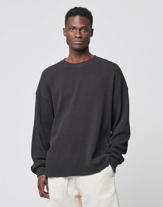 A man stands against a light gray background, wearing the LIVE FAST DIE YOUNG Basic Waffle Longsleeve in black (100% Baumwolle) and off-white pants, with one hand in his pocket and a neutral expression.
