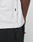 Close-up of a person wearing the LIVE FAST DIE YOUNG Basic Trademark Tee—a white, 100% Baumwolle oversized t-shirt with a small black side tag. Paired with black pants and a hand near the pocket for a minimal look.