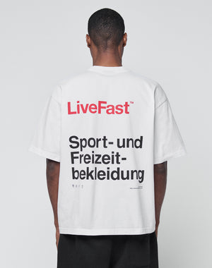 A person with short hair is seen from behind in a white Basic Trademark Tee by LIVE FAST DIE YOUNG, made of 100% cotton. The oversize fit features LiveFast in red and bold black Sport- und Freizeitbekleidung on the back.