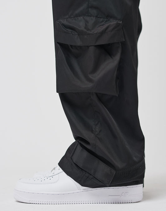 A close-up side view of a person wearing LIVE FAST DIE YOUNG Nylon Cargo pants with regular fit pockets, made from durable polyester, paired with white Nike Air Force 1 sneakers against a plain background.
