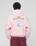 A person in an oversized light pink LIVE FAST DIE YOUNG Basic Evidence Hooded Zip, with repeated "LiveFast" text on the back, pairs it with maroon pants while standing facing away from the camera against a plain background.
