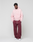 A person stands against a plain background wearing the LIVE FAST DIE YOUNG Basic Evidence Hooded Zip in light pink, paired with maroon sweatpants and white sneakers. Hands are in pockets, and they look relaxed.