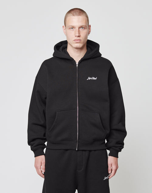 A person with short hair wears the LIVE FAST DIE YOUNG Basic Script Hooded Zip and matching black sweatpants, standing facing forward against a plain white background.