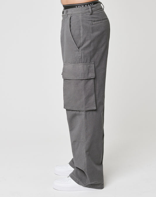 A person in LIVE FAST DIE YOUNG Wide Cargo high-waisted gray ripstop cargo pants with large pockets and a wide fit, styled with white sneakers, is shown in side profile against a plain white background.