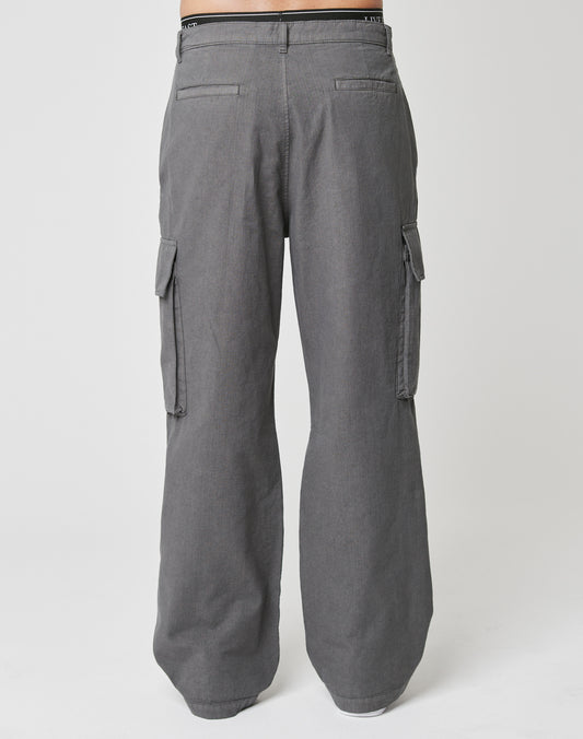 Back view of a person wearing LIVE FAST DIE YOUNG wide fit Wide Cargo pants in gray ripstop, featuring side flap cargo pockets and back welt pockets, standing against a plain white background.