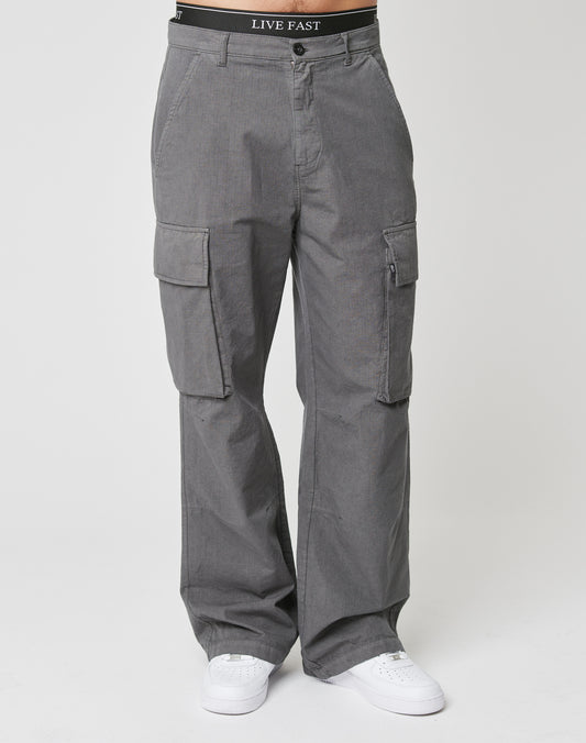 A person wears the LIVE FAST DIE YOUNG Wide Cargo in gray ripstop with cargo pockets and white sneakers. The black LIVE FAST waistband is visible above the pants against a plain white background.
