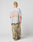 A person in an oversize fit gray LIVE FAST DIE YOUNG LFDY Praying Tee with a bold orange backprint, beige beanie, and baggy camouflage pants stands facing away from the camera against a plain light gray background.