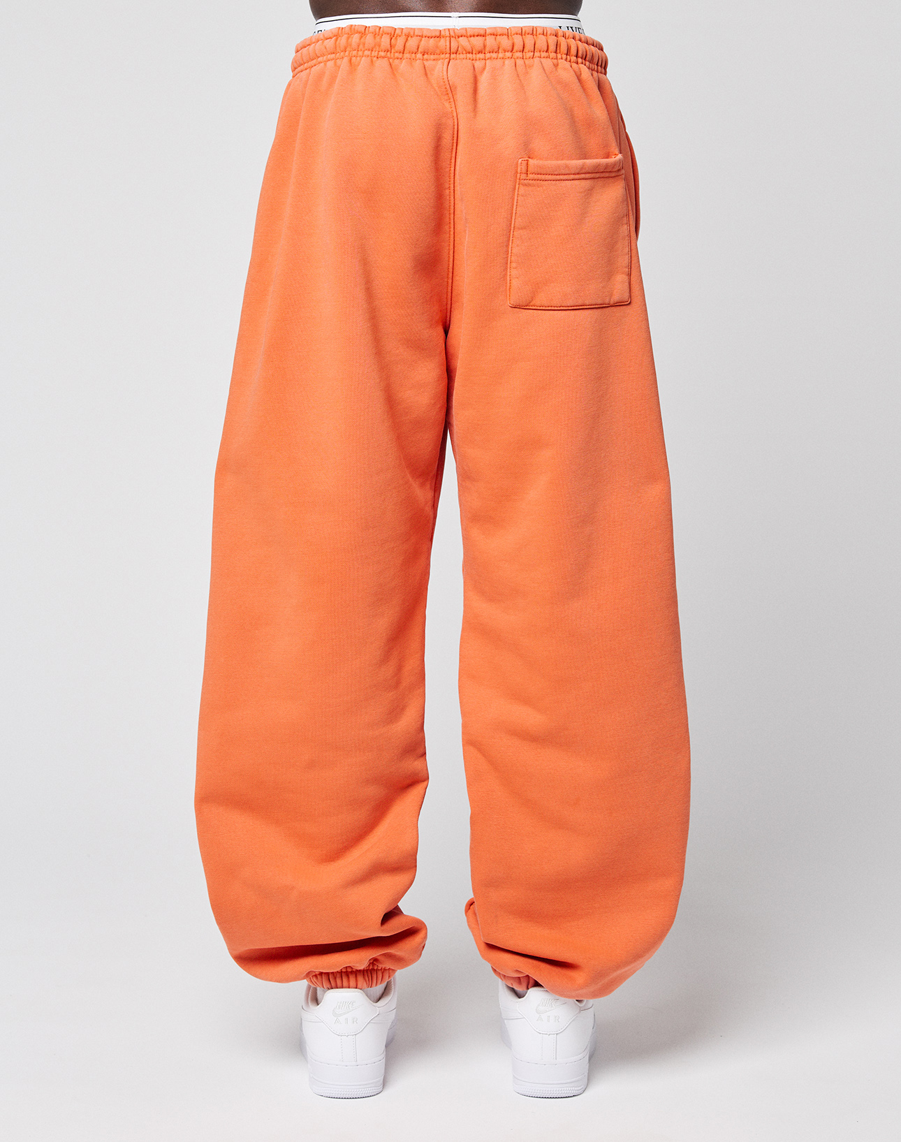 A person wears LIVE FAST DIE YOUNG's LFDY 40 Wide Cuff Jogger—loose-fitting, bright orange sweatpants with side pockets, an elastic waistband, and a back pocket. Only the lower body and white sneakers are shown against a plain white background.