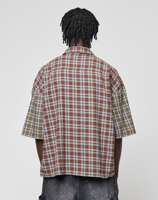 A person with short, twisted hair is seen from behind wearing the LIVE FAST DIE YOUNG LFDY Light Flannel—an oversized, short-sleeved plaid shirt in brown and green—paired with dark denim shorts against a plain background.