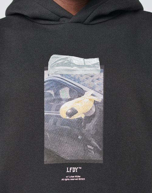 The Mirror Hooded by LIVE FAST DIE YOUNG is a black oversized hoodie featuring a car door handle with yellow tape and a folded bill frontprint, LFDY™ branding, photo credits below, and a subtle 3D tactile effect.