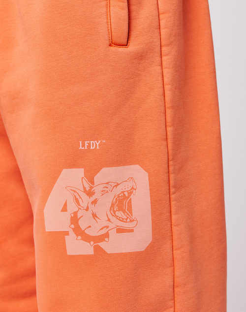 Close-up of the LFDY 40 Wide Cuff Jogger by LIVE FAST DIE YOUNG in orange Oversize Fit, featuring a printed 43, snarling dog graphic with spiked collar, LFDY text above, and side pockets.