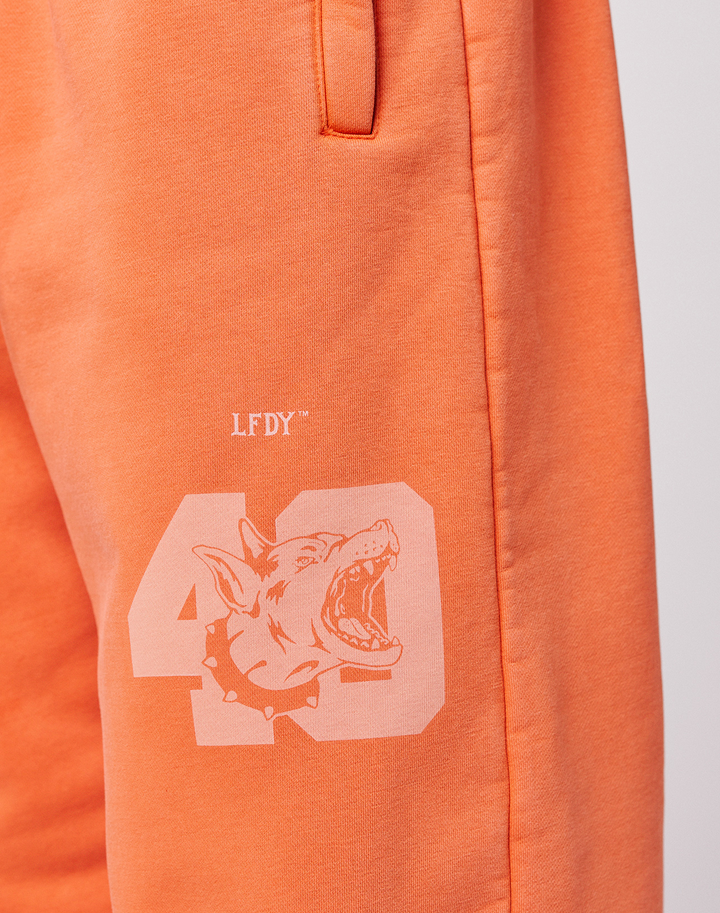 Close-up of the LFDY 40 Wide Cuff Jogger by LIVE FAST DIE YOUNG in orange Oversize Fit, featuring a printed 43, snarling dog graphic with spiked collar, LFDY text above, and side pockets.