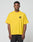 A man stands facing forward wearing the LFDY Circle Dog Tee by LIVE FAST DIE YOUNG, a loose-fitting yellow oversize t-shirt with a small black LFYT graphic on the upper left chest, made from 100% cotton, paired with black pants against a light gray background.