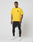 A man stands against a plain white background, wearing the LIVE FAST DIE YOUNG LFDY Circle Dog Tee in yellow (Oversize Fit), black shorts, black leggings, and white sneakers. He looks forward neutrally with his arms relaxed by his sides.
